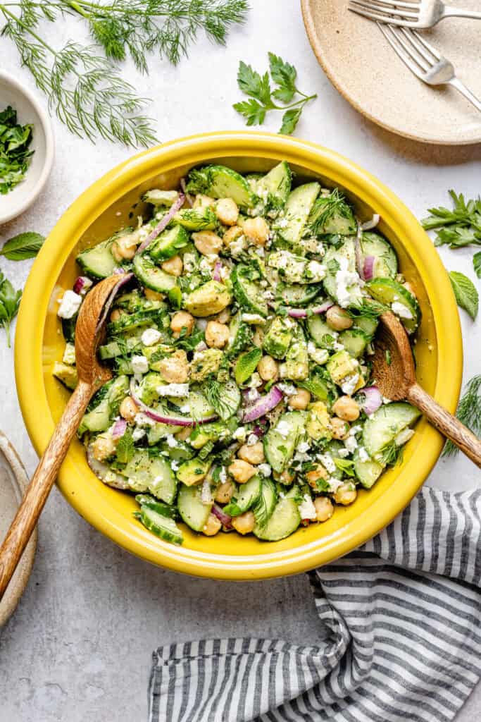 cucumber chickpea salad in mixing bowl with wooden spoons