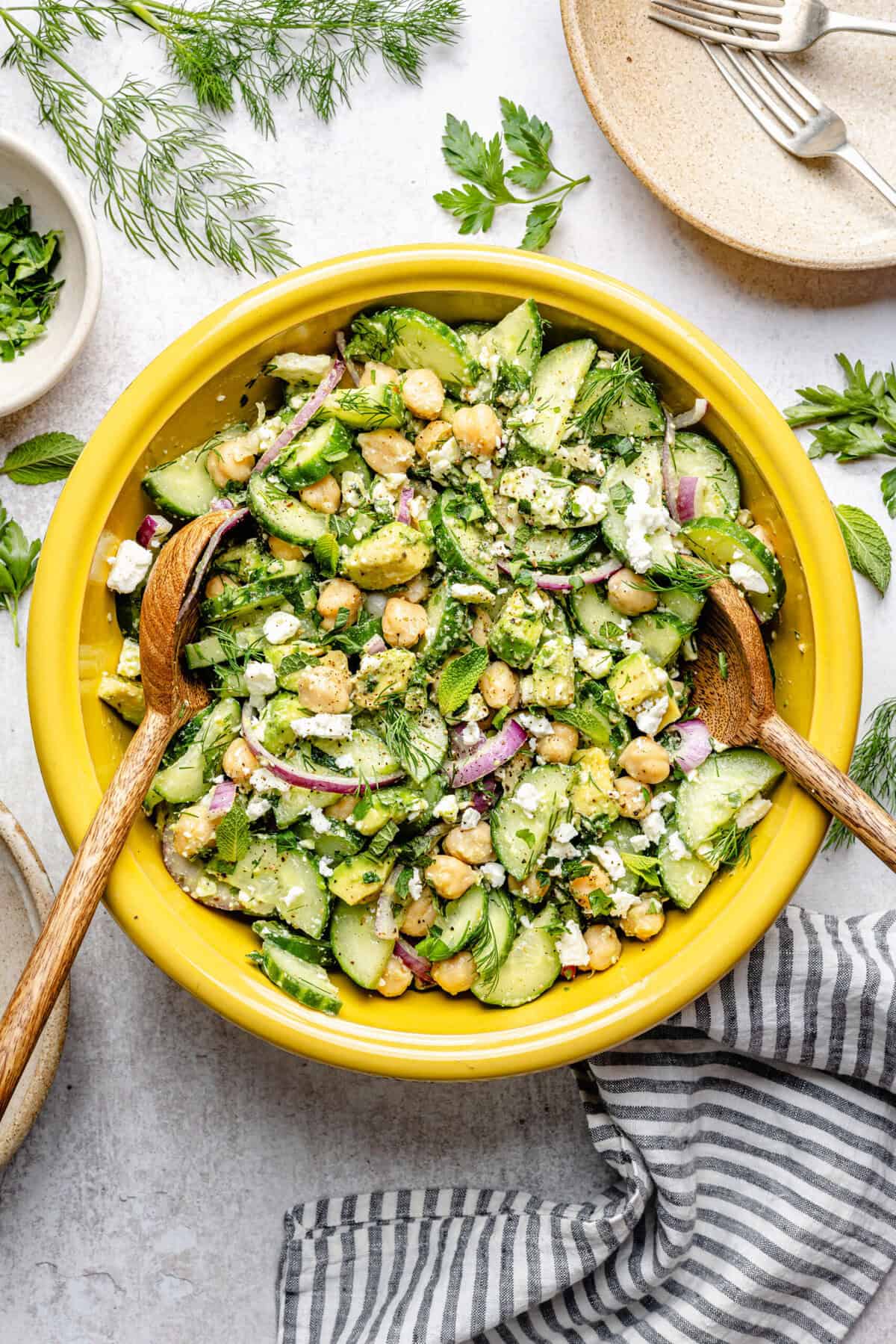 cucumber chickpea salad in mixing bowl with wooden spoons