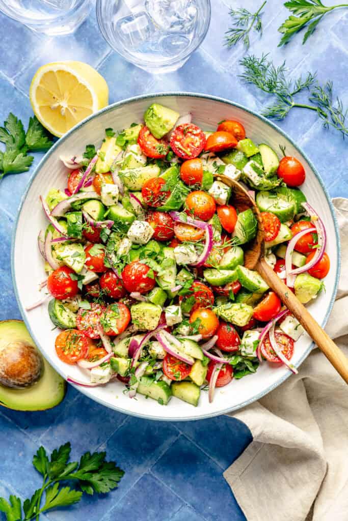 tomato cucumber avocado salad in serving bowl with serving spoon
