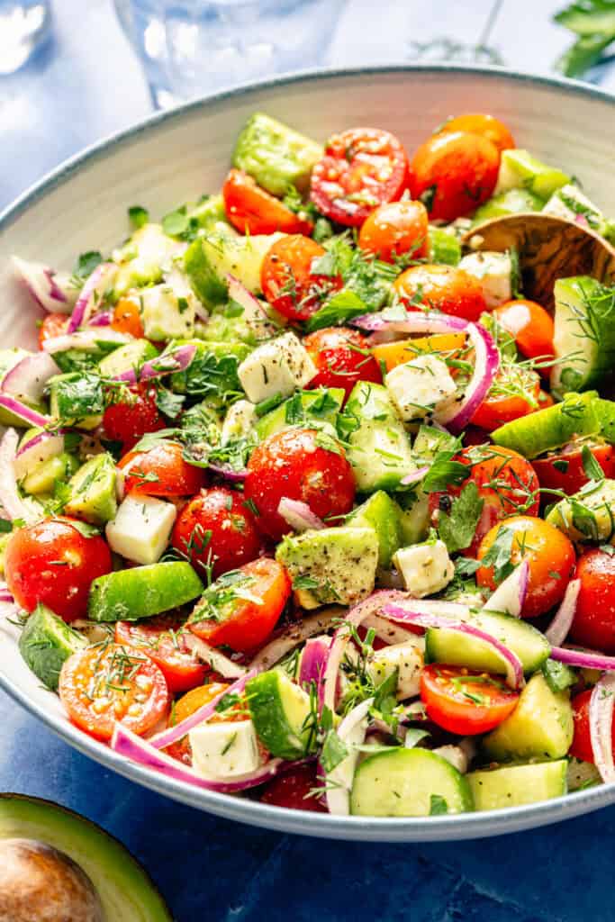 tomato cucumber avocado salad in a bowl with serving spoon 